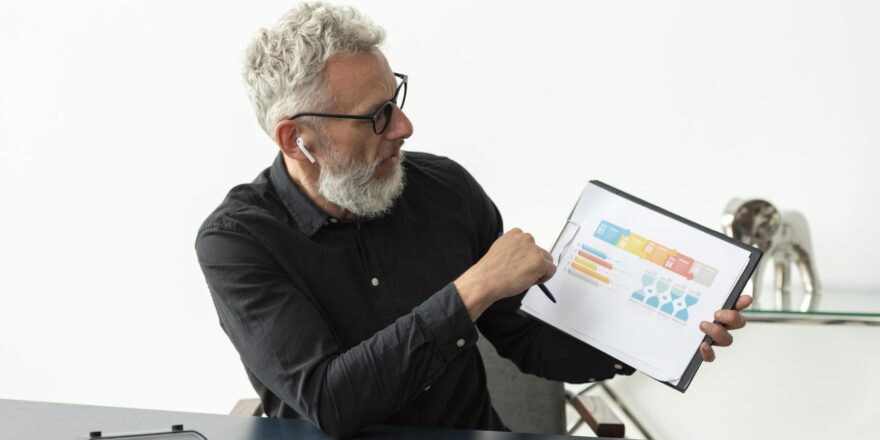 older-man-home-showing-graph-notepad-with-tablet-desk